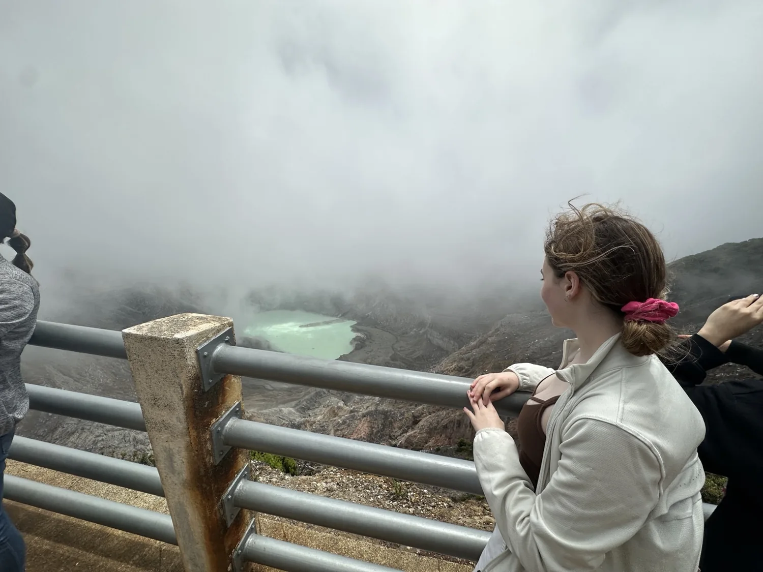 Lyra looking toward a pale turquoise volcanic crater lake through mist